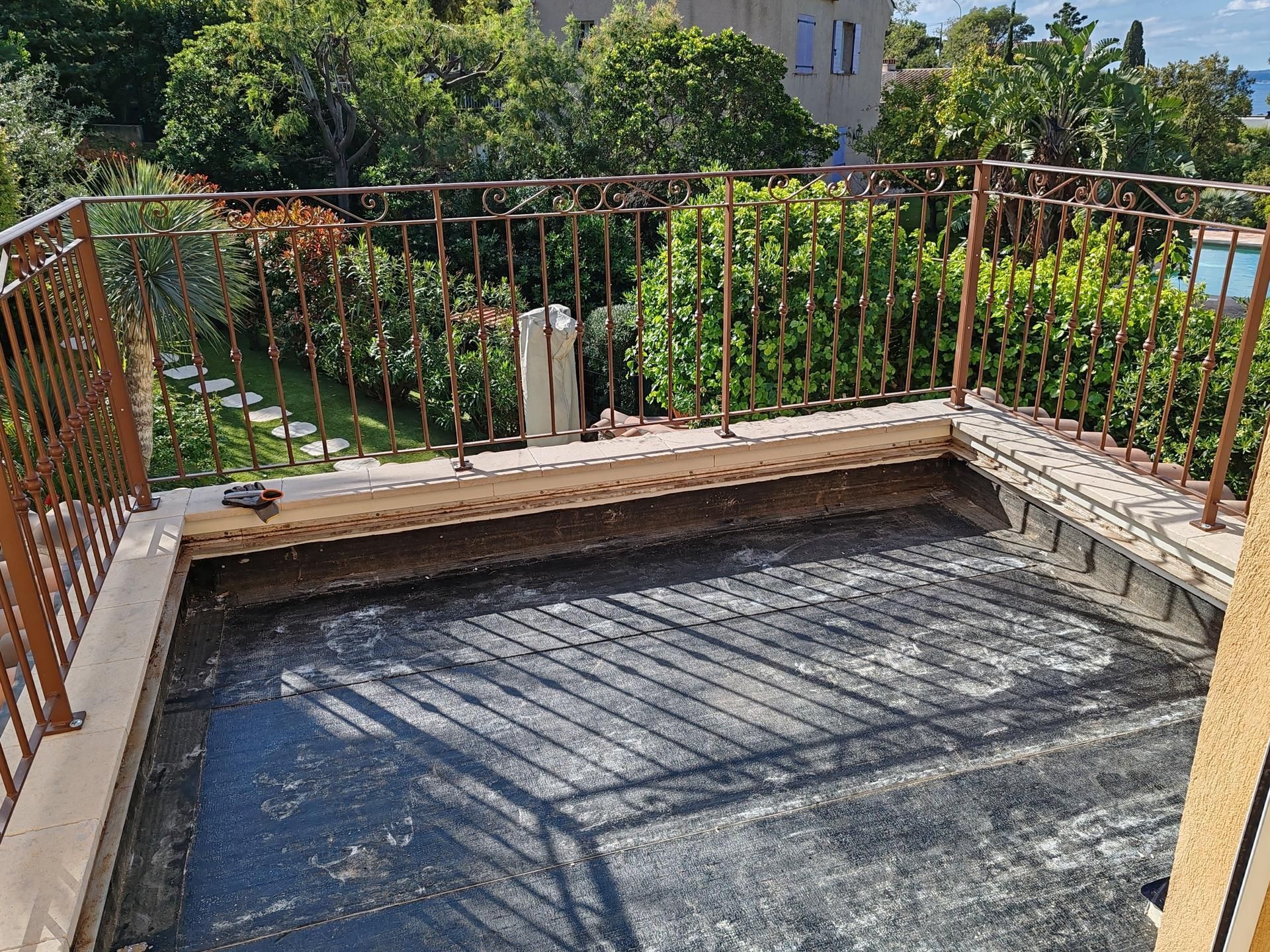 Une terrasse extérieure en cours de rénovation avec un sol en membrane d'étanchéité noire apparente et une balustrade décorative en métal.