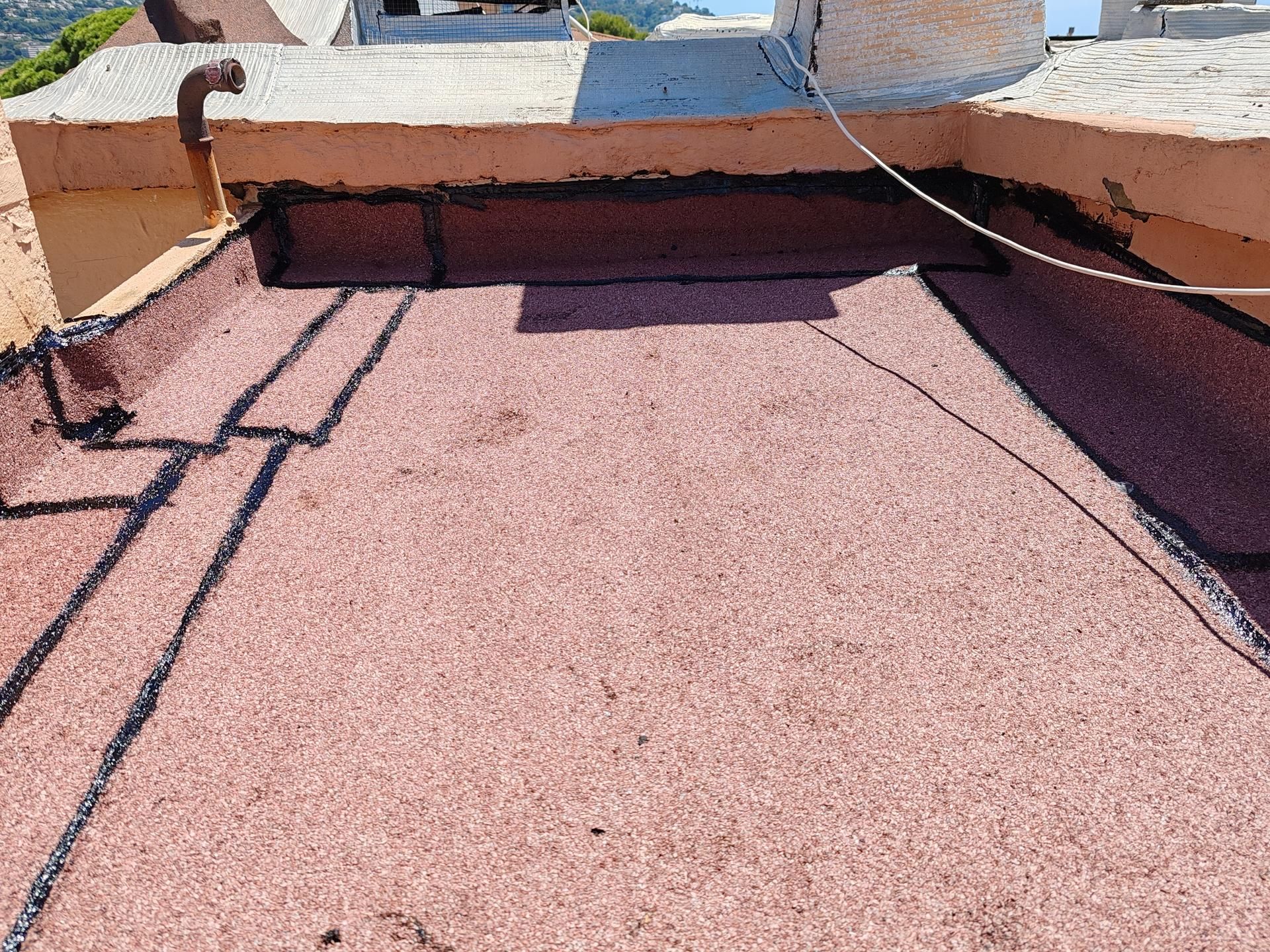 Un toit plat recouvert d'un matériau de couverture minéral rosé et d'un mastic noir sur les bords et à la base des murs.