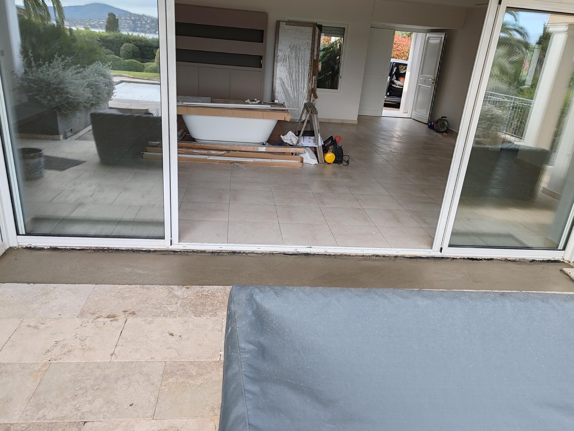 Vue depuis une terrasse donnant sur, à travers des portes coulissantes en verre, une pièce en cours de rénovation avec une nouvelle baignoire blanche.