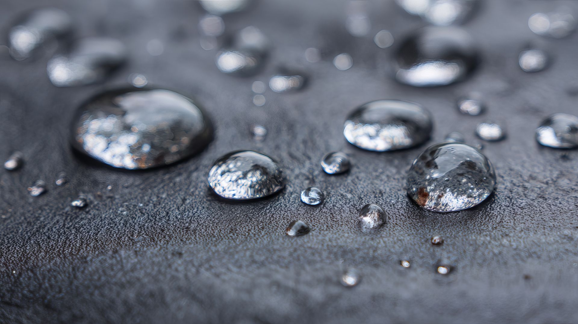 Des gouttelettes d'eau de tailles variées reposent sur une surface sombre et texturée.