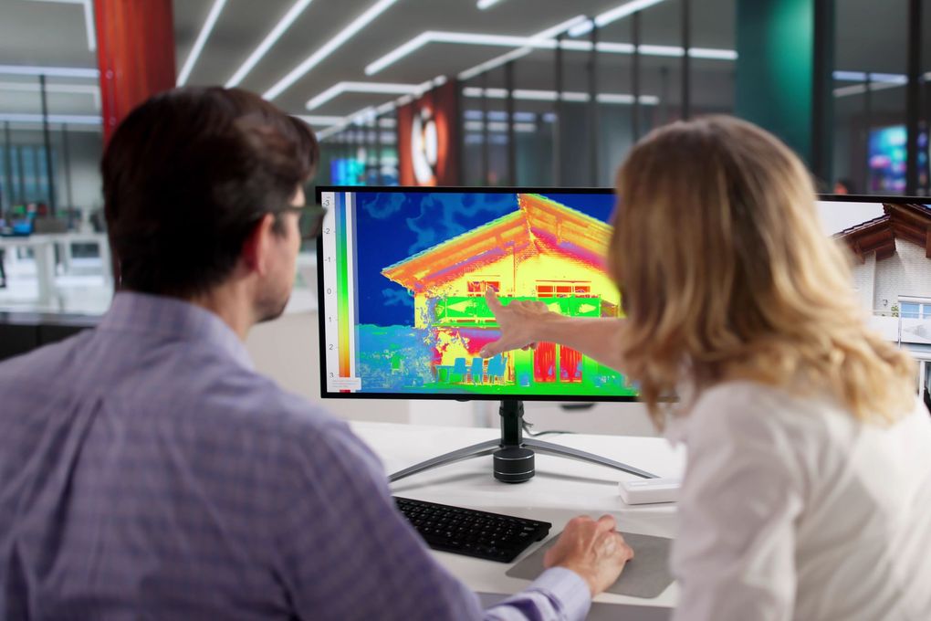 Deux personnes consultent une image thermique d'une maison sur un écran d'ordinateur.