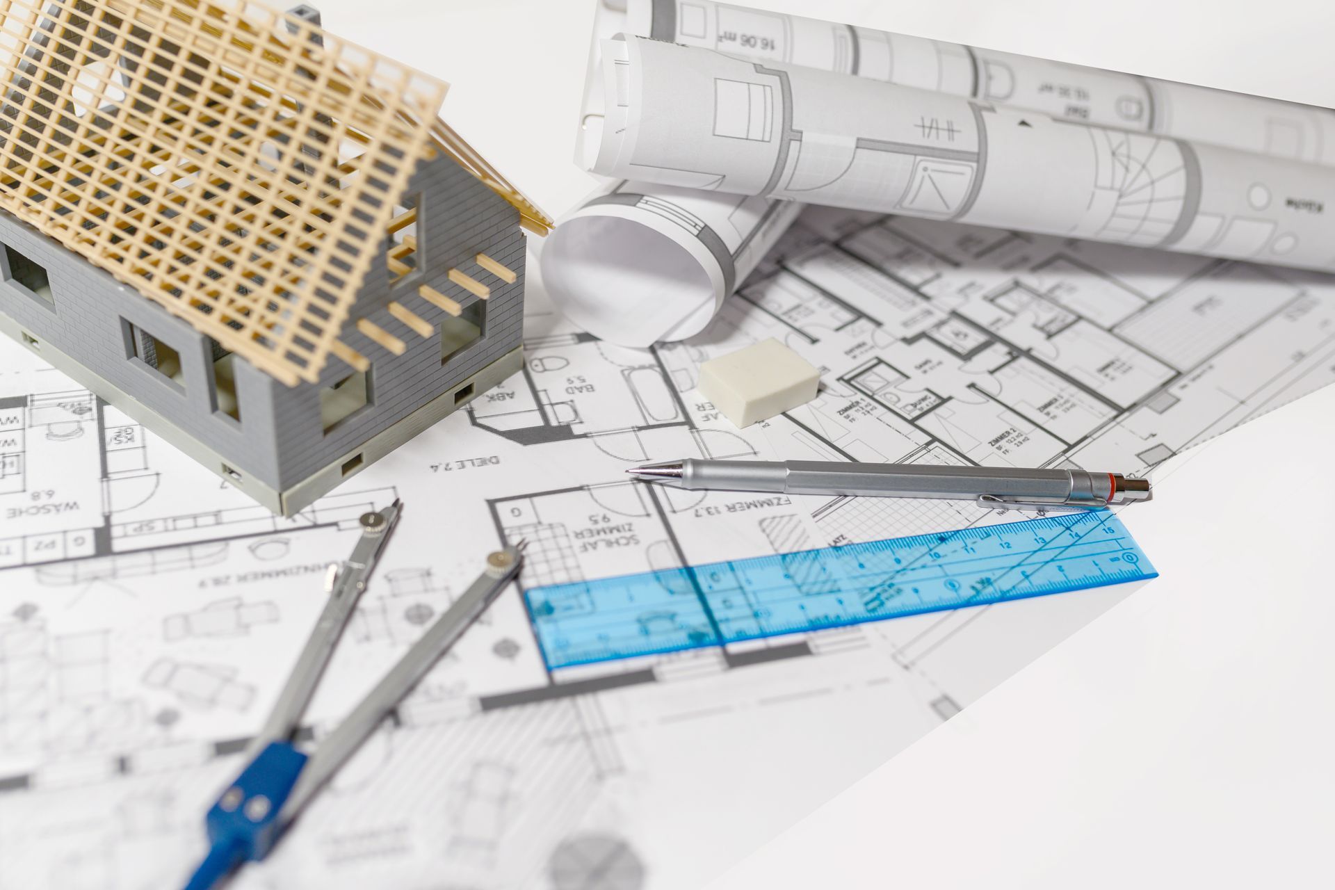 Plan architectural avec maquette de maison, règle, crayon et plans enroulés sur un bureau.