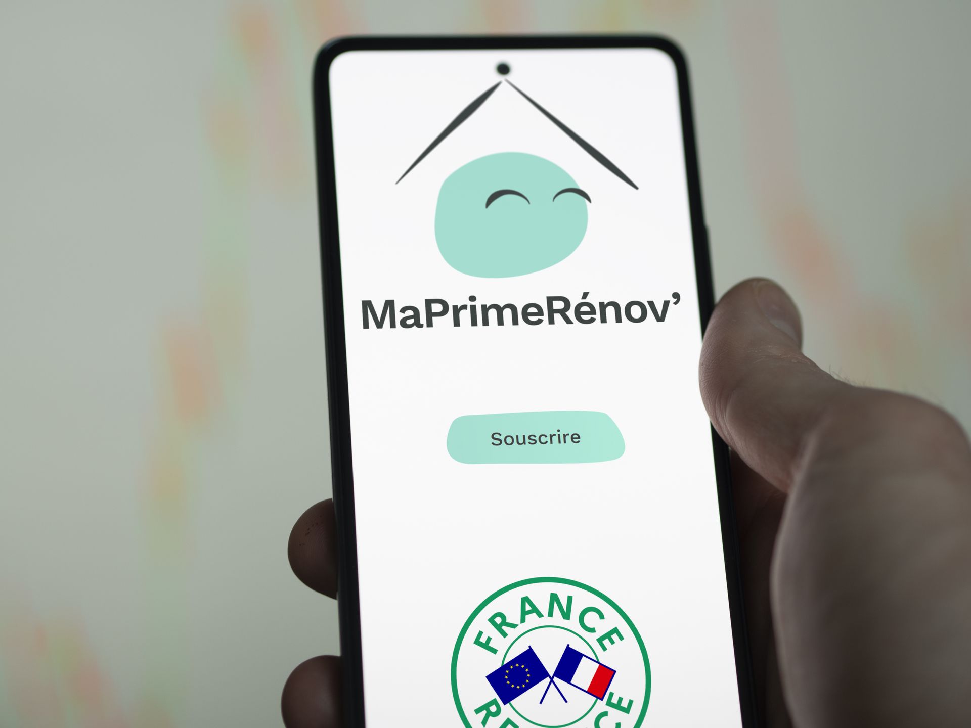 Une main tenant un téléphone avec le logo de MaPrimeRénov.