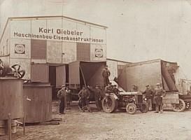 Eine Gruppe Männer steht neben einem Traktor vor einem Gebäude.