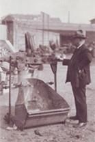 Ein Mann in Anzug und Hut steht neben einem großen Metallgegenstand.