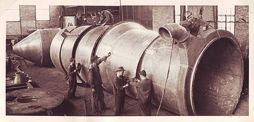 Eine Gruppe Männer arbeitet in einer Fabrik an einem großen Rohr.