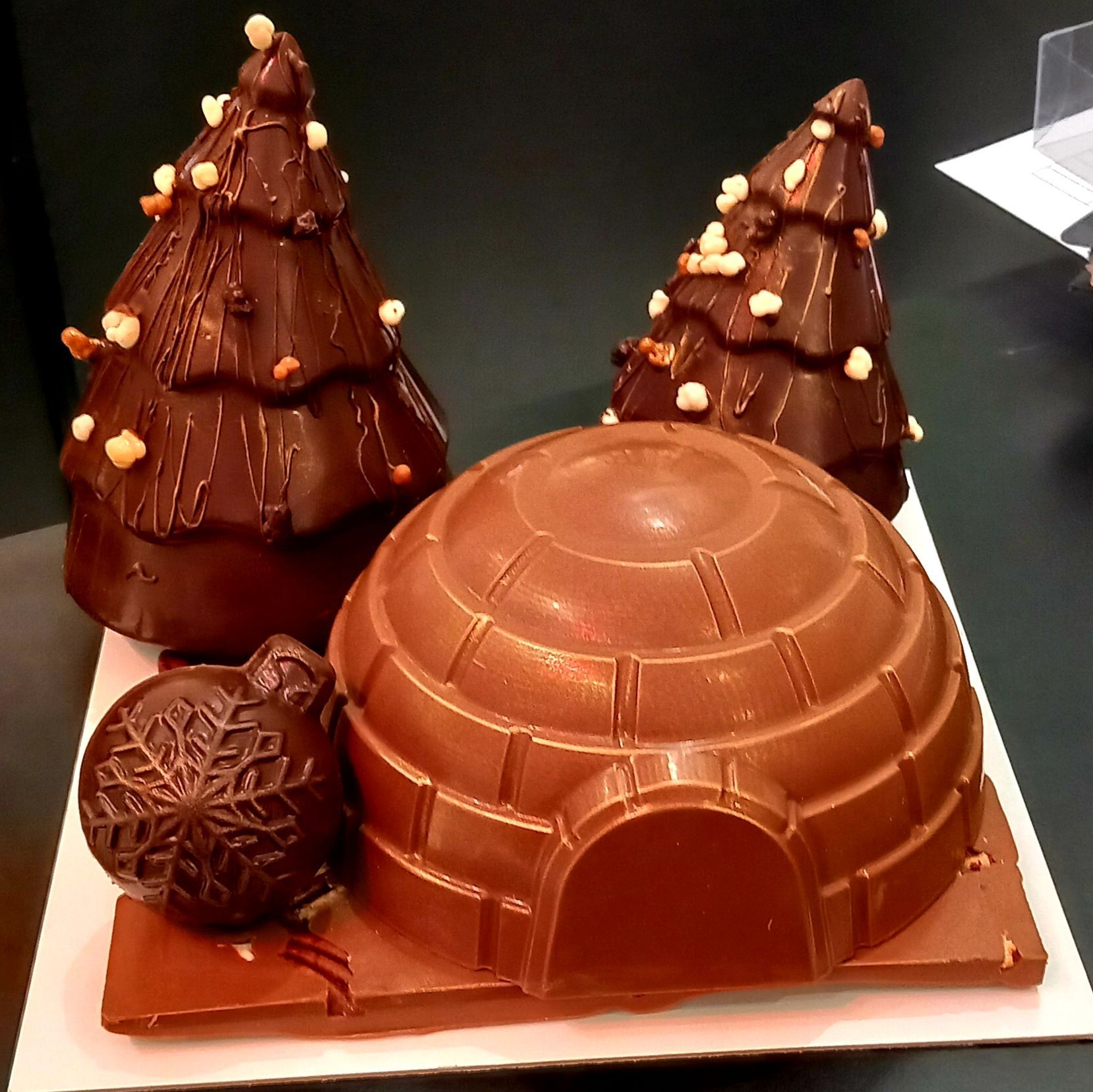 Scène de Noël en chocolat : arbres avec noix, iglou, ornement, le tout sur une base en chocolat.