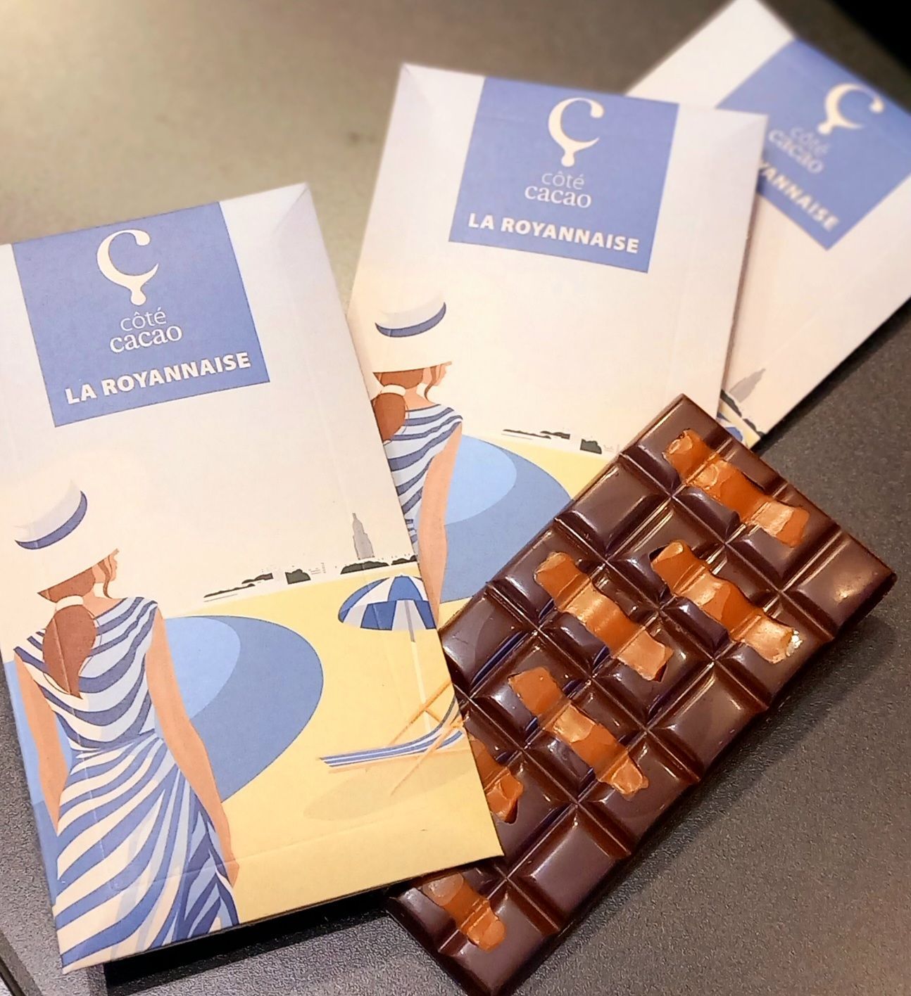 Tablette de chocolat et emballage représentant une femme en robe rayée à la plage ; bleu, blanc, marron.