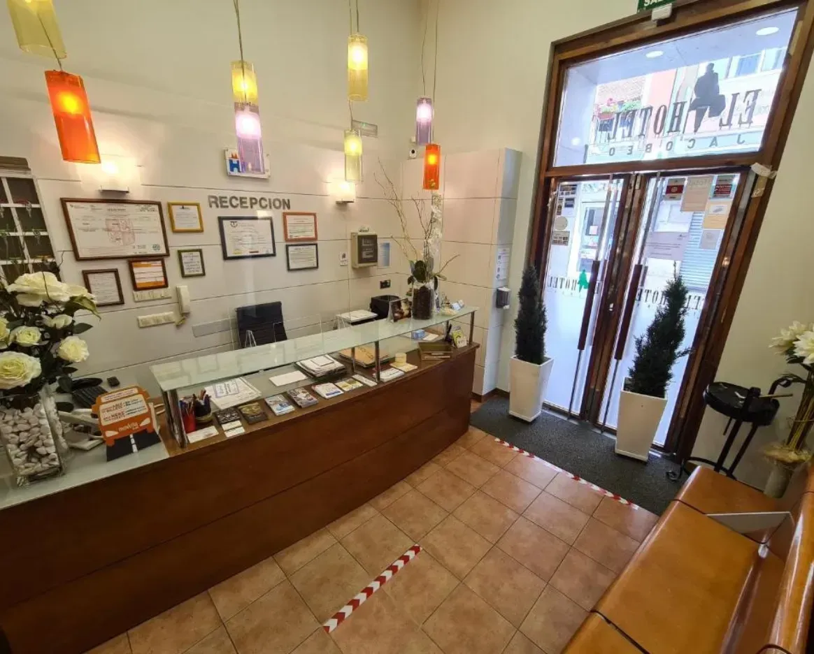 Mostrador de recepción de hotel con mostrador de madera, puertas abiertas al exterior, iluminación cenital.