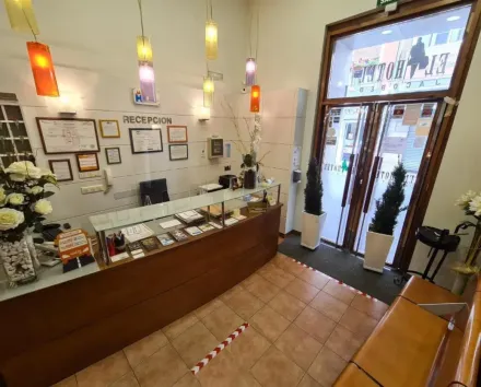 Mostrador de recepción de hotel con mostrador de madera, puertas abiertas al exterior, iluminación cenital.