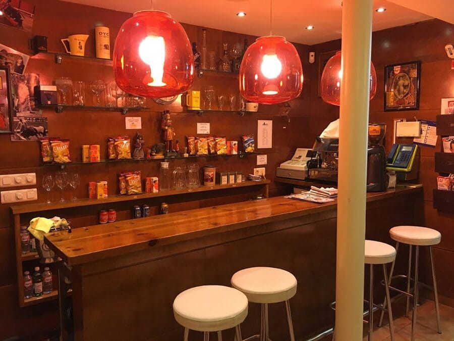 Un restaurante con barra y taburetes con luces rojas colgando del techo.