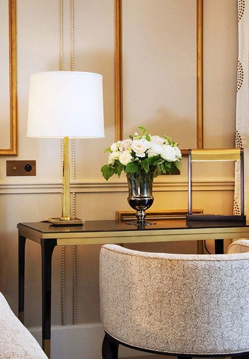 Un jarrón de flores reposa sobre una mesa al lado de una lámpara.