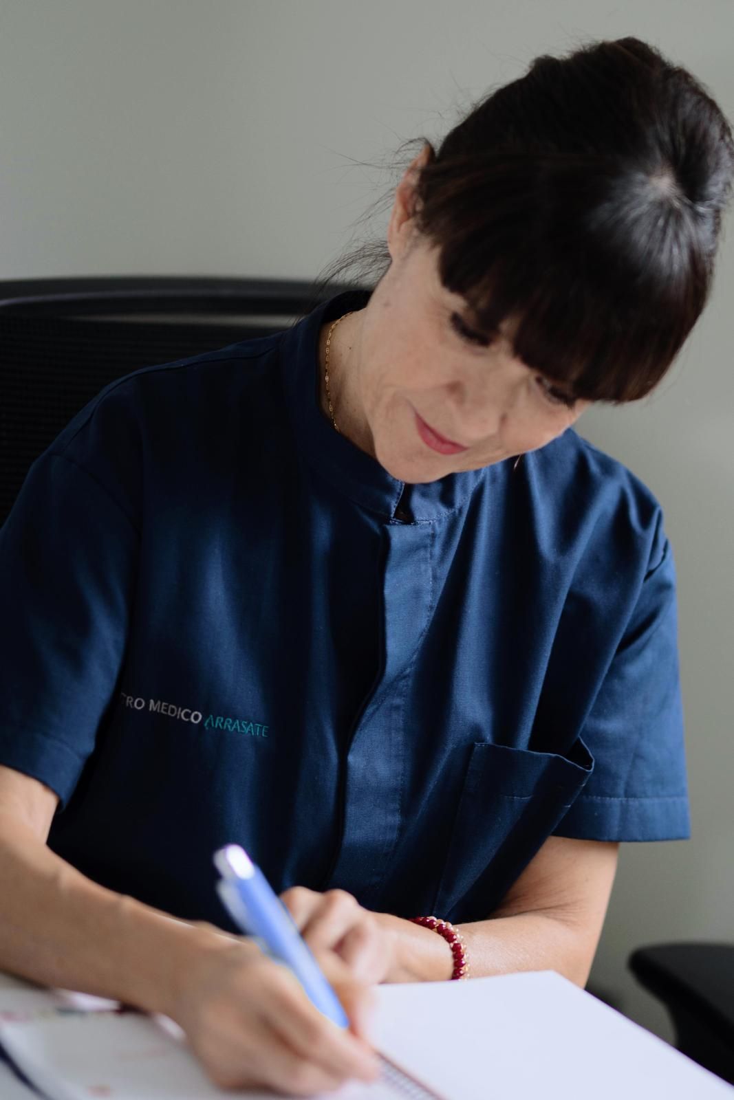 Mujer escribiendo en un papel; lleva una camisa azul con cuello.