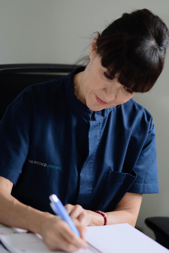Mujer escribiendo en un papel; lleva una camisa azul con cuello.