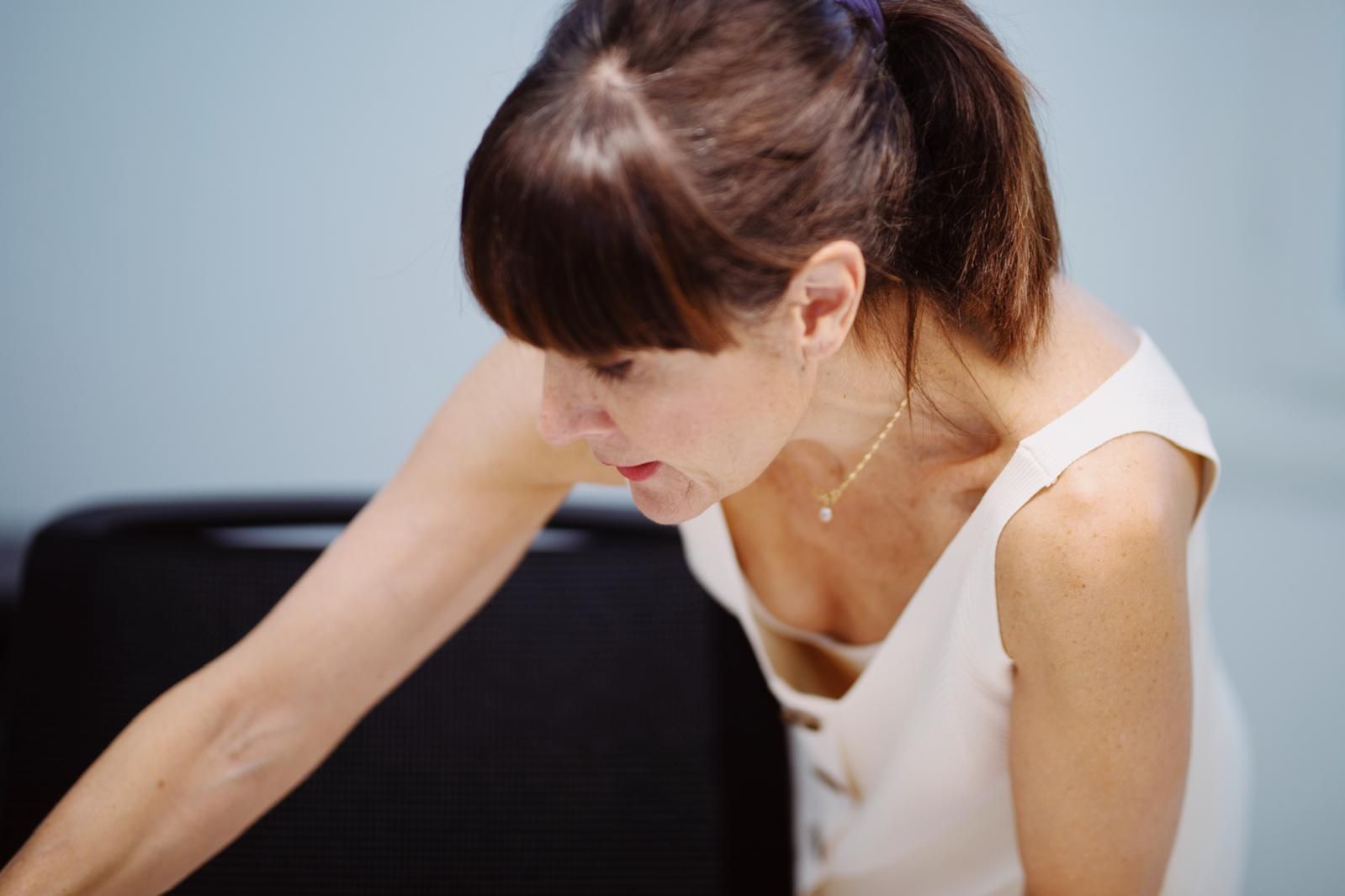 Una mujer, vestida con un vestido de color claro, se inclina hacia adelante y mira hacia abajo