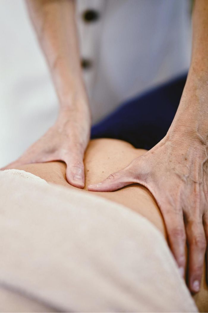 Manos realizando un masaje en la zona lumbar de una persona, sobre una camilla de masaje.