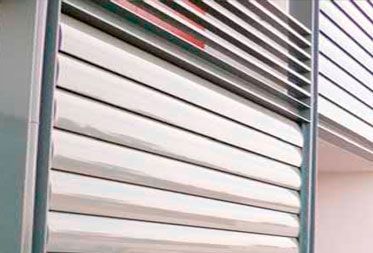 Persianas modernas de lamas metálicas en tono plateado instaladas en la fachada de un edificio.