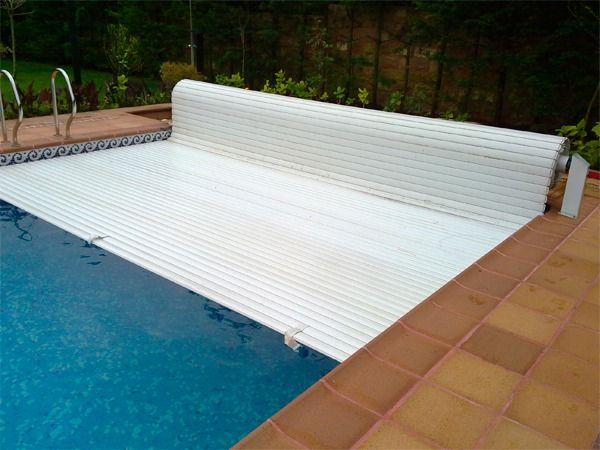 Una cubierta retráctil blanca se extiende parcialmente sobre una piscina azul situada en un patio pavimentado.