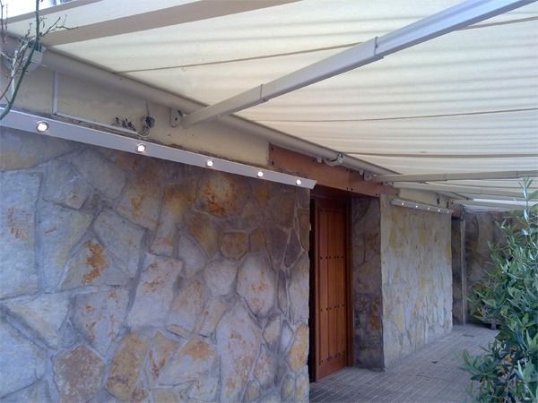 Un muro exterior de piedra con un moderno toldo retráctil blanco con luces LED integradas sobre una puerta de madera.