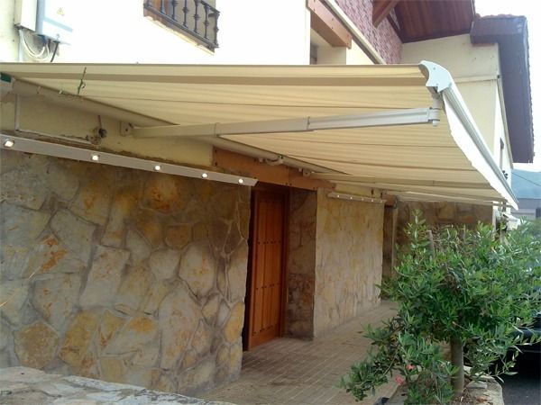 Un toldo retráctil de color beige se extendía sobre la entrada de piedra de una casa, con una guirnalda de luces integrada.