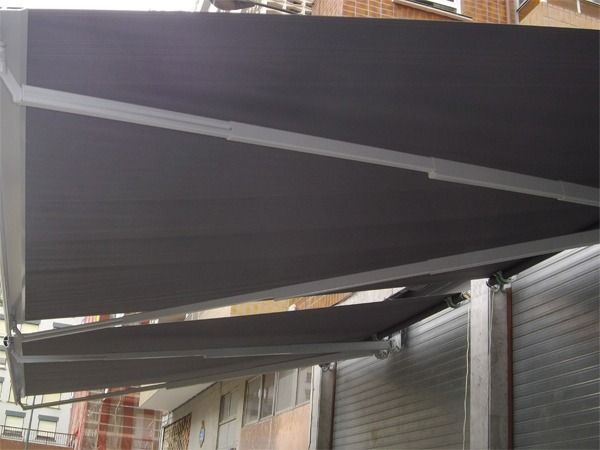 Dos toldos retráctiles negros de gran tamaño, instalados sobre un edificio de ladrillo y una fachada metálica cerrada.