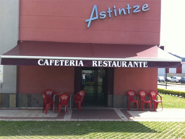 La cafetería y restaurante Astintze presenta una fachada roja, un toldo con texto blanco y asientos al aire libre.