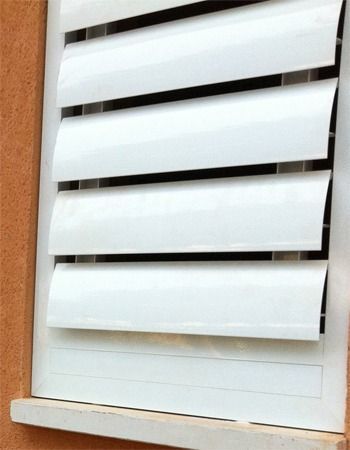 Vista de cerca de unas persianas blancas horizontales con lamas, integradas en una pared exterior de color naranja claro.