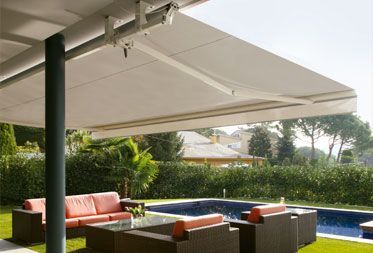 Un patio con muebles de exterior, una piscina rectangular y un toldo blanco retráctil que se extiende sobre la zona de estar.