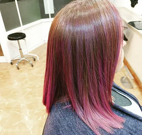 Una mujer con cabello morado está sentada en una silla en un salón.