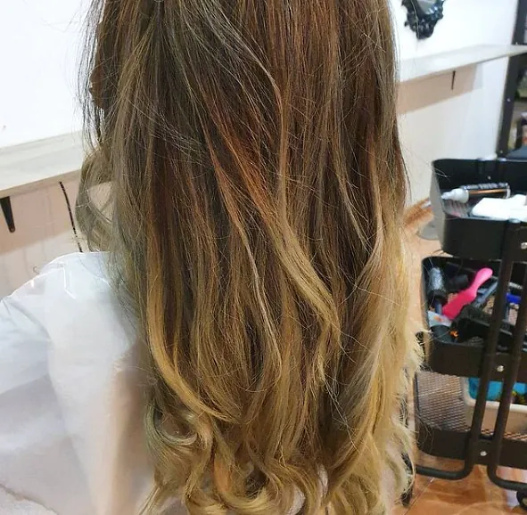 Una mujer con cabello largo y rubio está sentada en una silla en un salón.