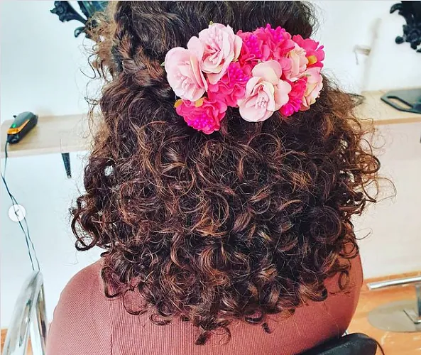 Una mujer con cabello rizado tiene flores rosas en el cabello.