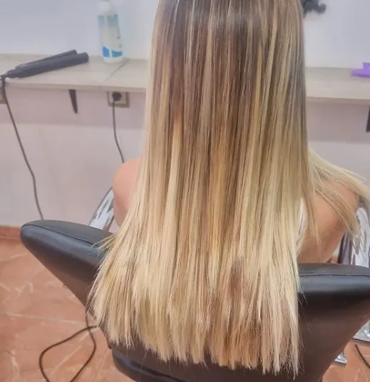 Una mujer con cabello largo y rubio está sentada en una silla.