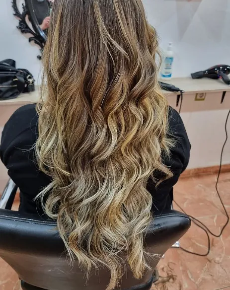 Una mujer con cabello largo y rubio está sentada en una silla en un salón.