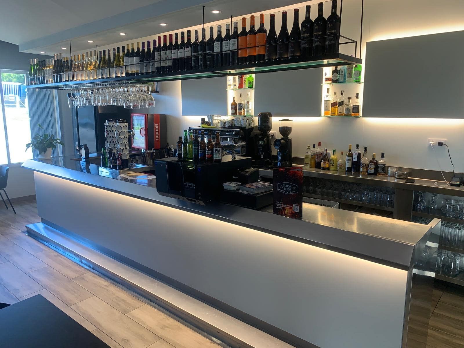 Barra con botellas, copas y mostrador iluminado.