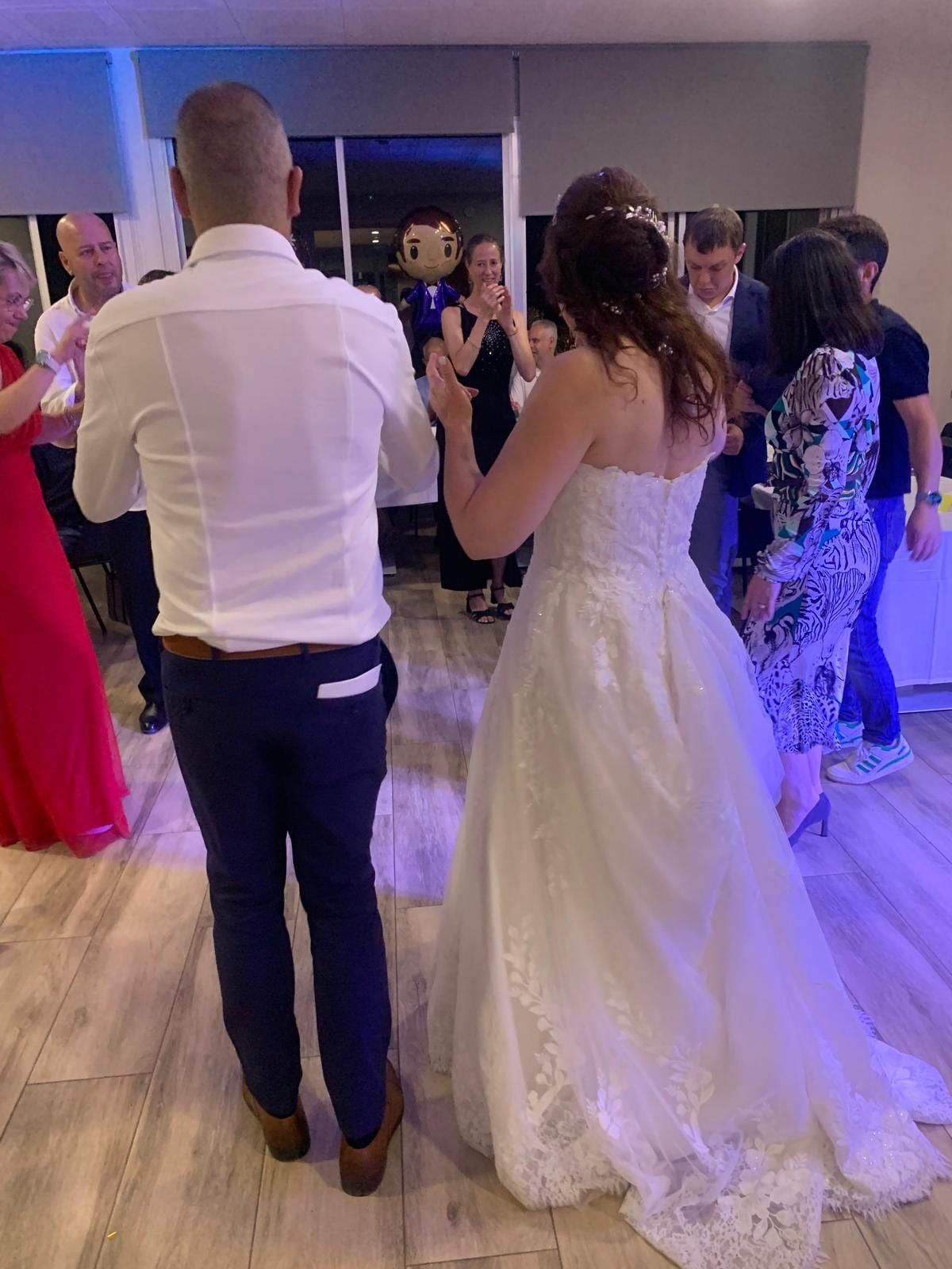 Una pareja bailando en una recepción de boda; otros invitados observaban. La novia con vestido blanco, el novio con camisa blanca y pantalón azul marino.