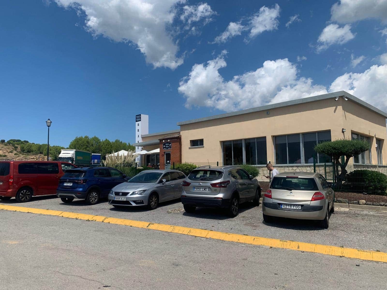 Coches aparcados delante de un edificio beige con grandes ventanales en un día soleado con cielo azul y nubes.