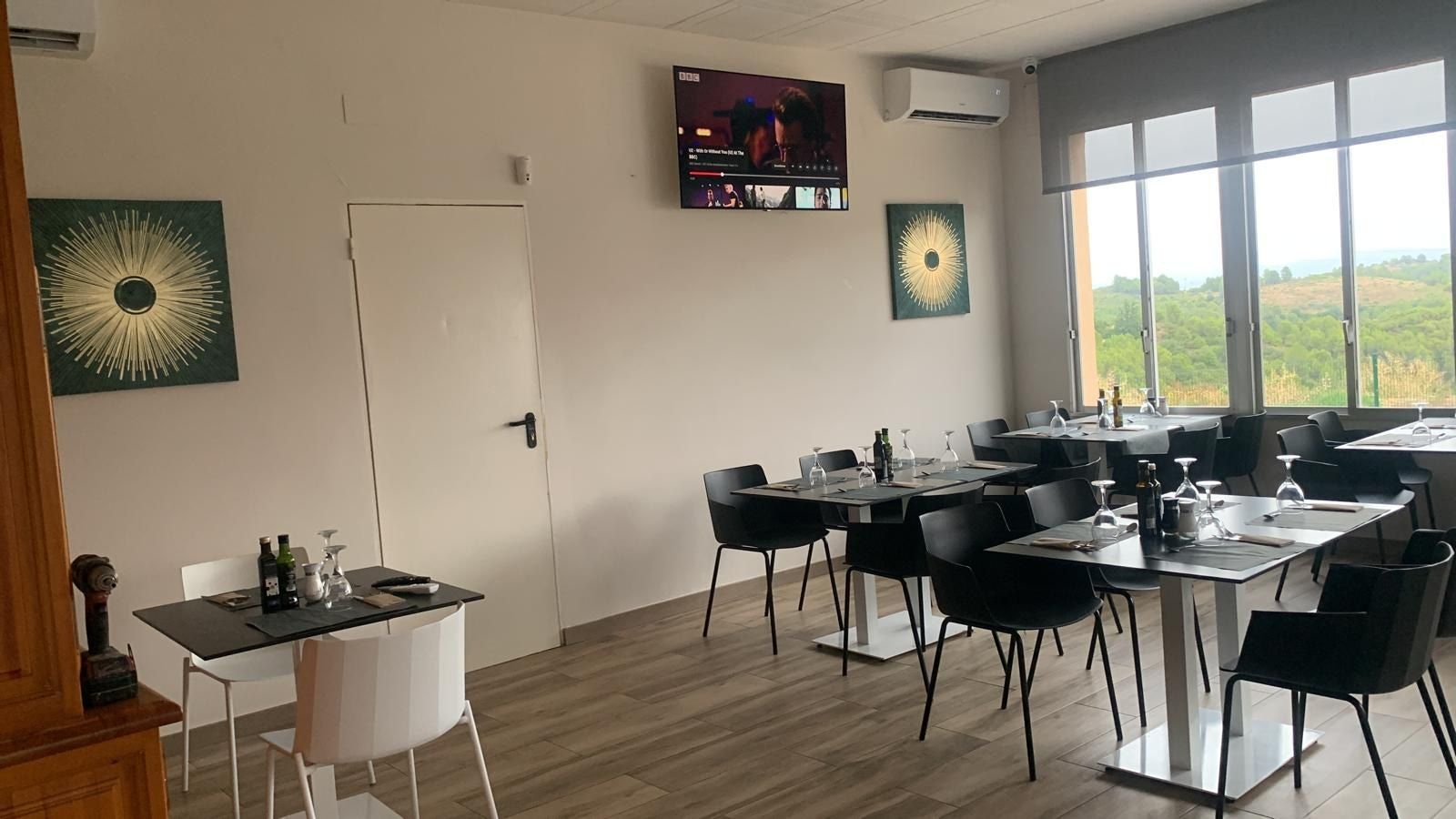 Interior de restaurante con mesas y sillas. Cuadros en la pared y una ventana con vistas.