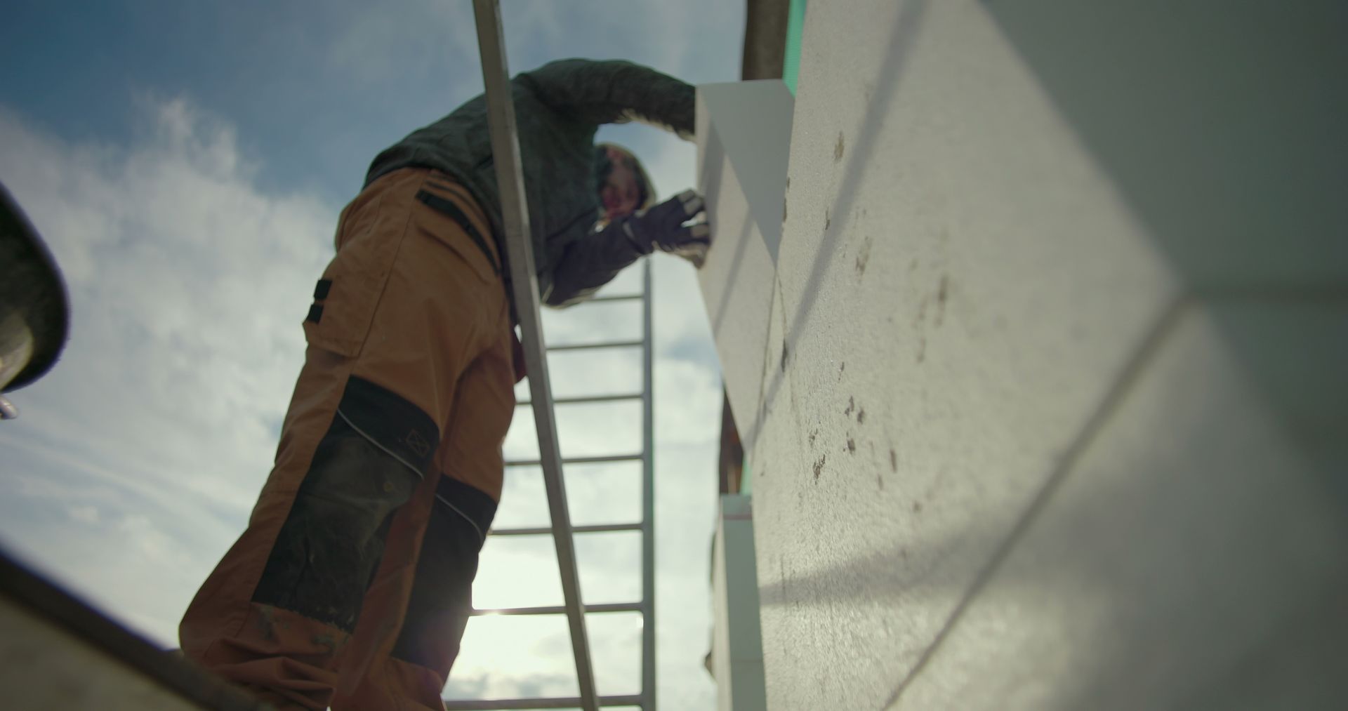 Ouvrier du bâtiment sur une échelle, appliquant un isolant extérieur sur une maison résidentielle.