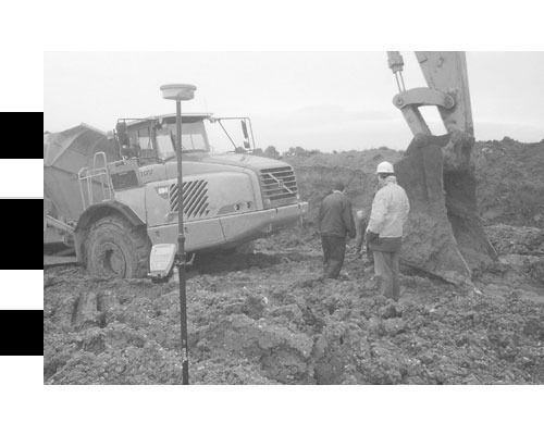Una fotografía en blanco y negro de un sitio de construcción con una excavadora y trabajadores.