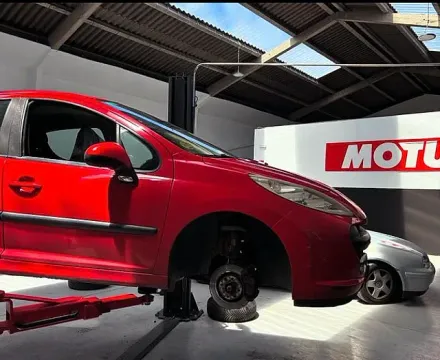 Un coche rojo está en un elevador frente a un cartel de Motul.