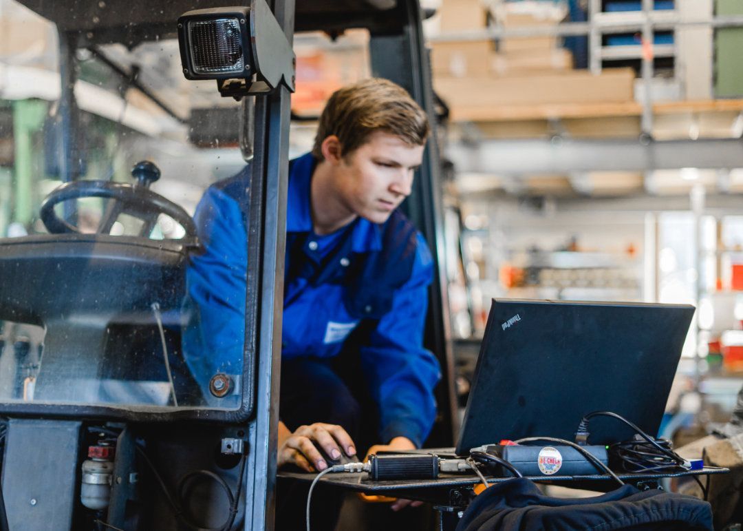 Mitarbeiter sitzt in einem Gabelstapler und macht mit dem Laptop eine Fehlerdiagnose