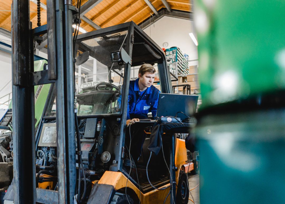 Mitarbeiter sitzt in einem Gabelstapler und macht mit dem Laptop eine Fehlerdiagnose
