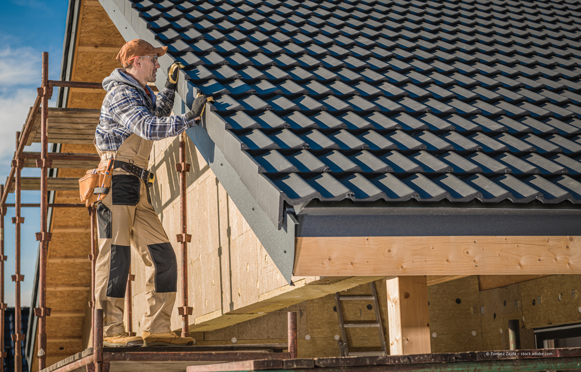 Arbeiter auf einem Gerüst bei der Montage von Dachplatten an einem im Bau befindlichen Haus.