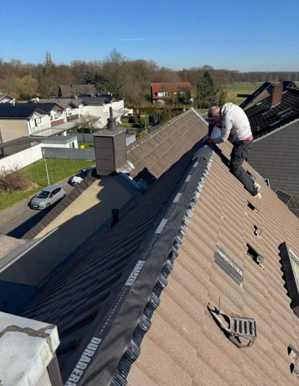 Ein Arbeiter repariert auf einem braunen Schindeldach in einem Vorstadtviertel die Dachziegel.