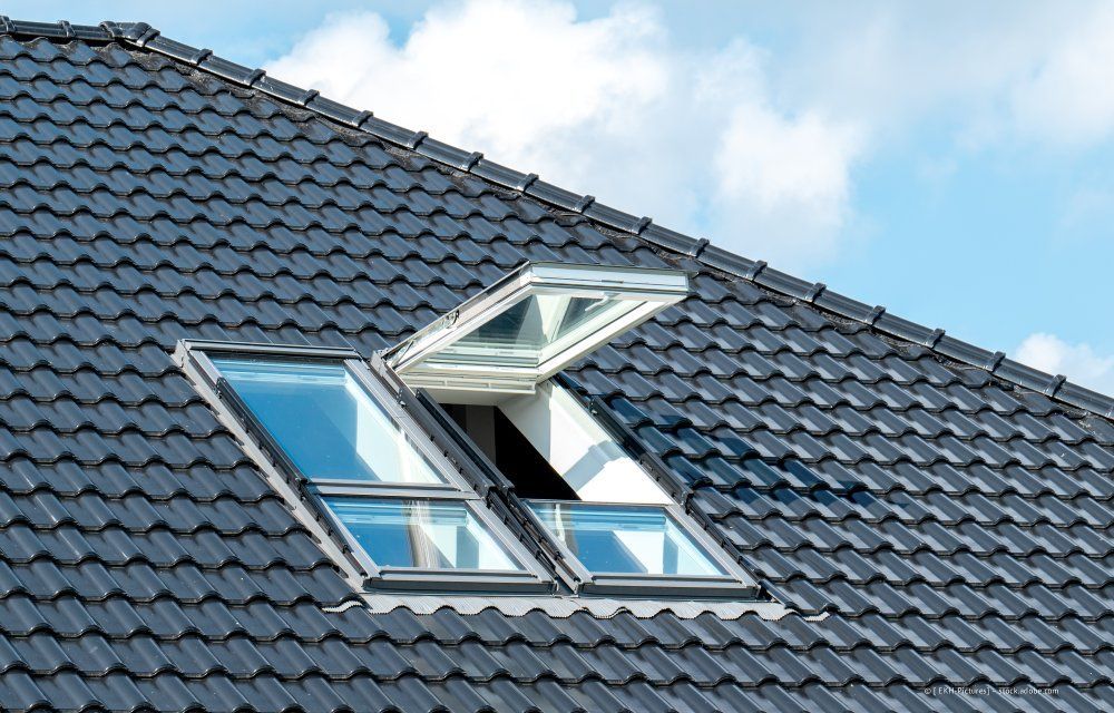 Offenes Dachfenster auf einem dunkelgrauen Ziegeldach vor blauem Himmel