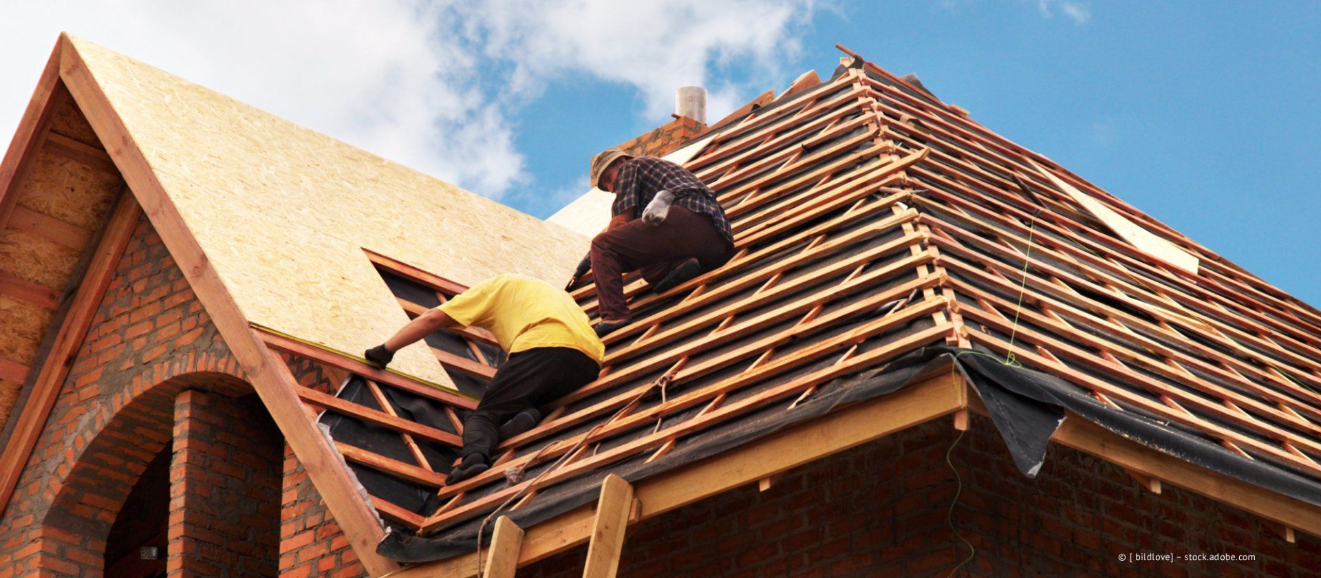 Dachdecker arbeiten an einem Hausdach mit roten Schindeln unter blauem Himmel