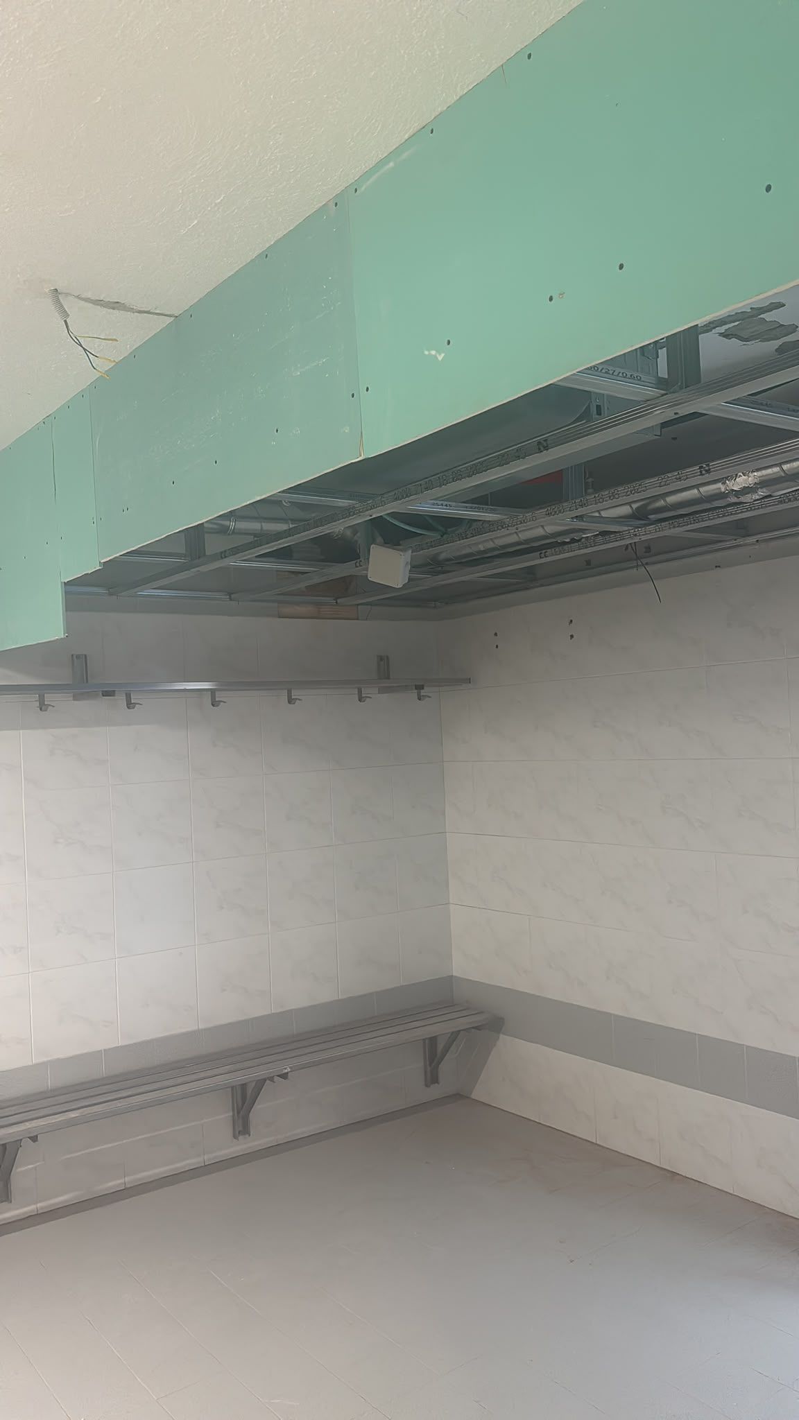 Un cuarto de servicio vacío con paredes blancas, paneles de techo verde menta y estantes metálicos a los lados.