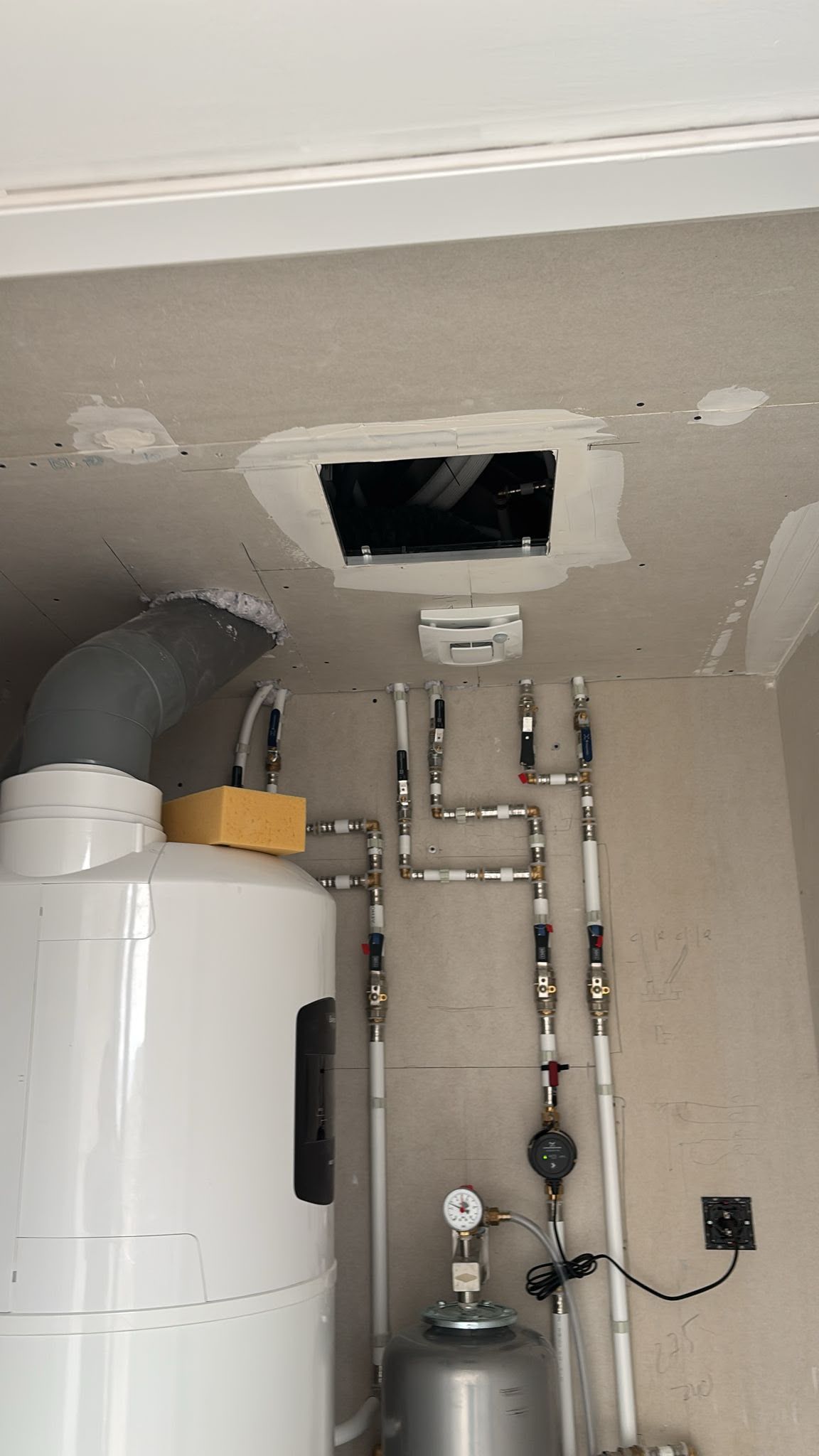 Cuarto de servicio con calentador de agua, tuberías y una abertura de ventilación en el techo.