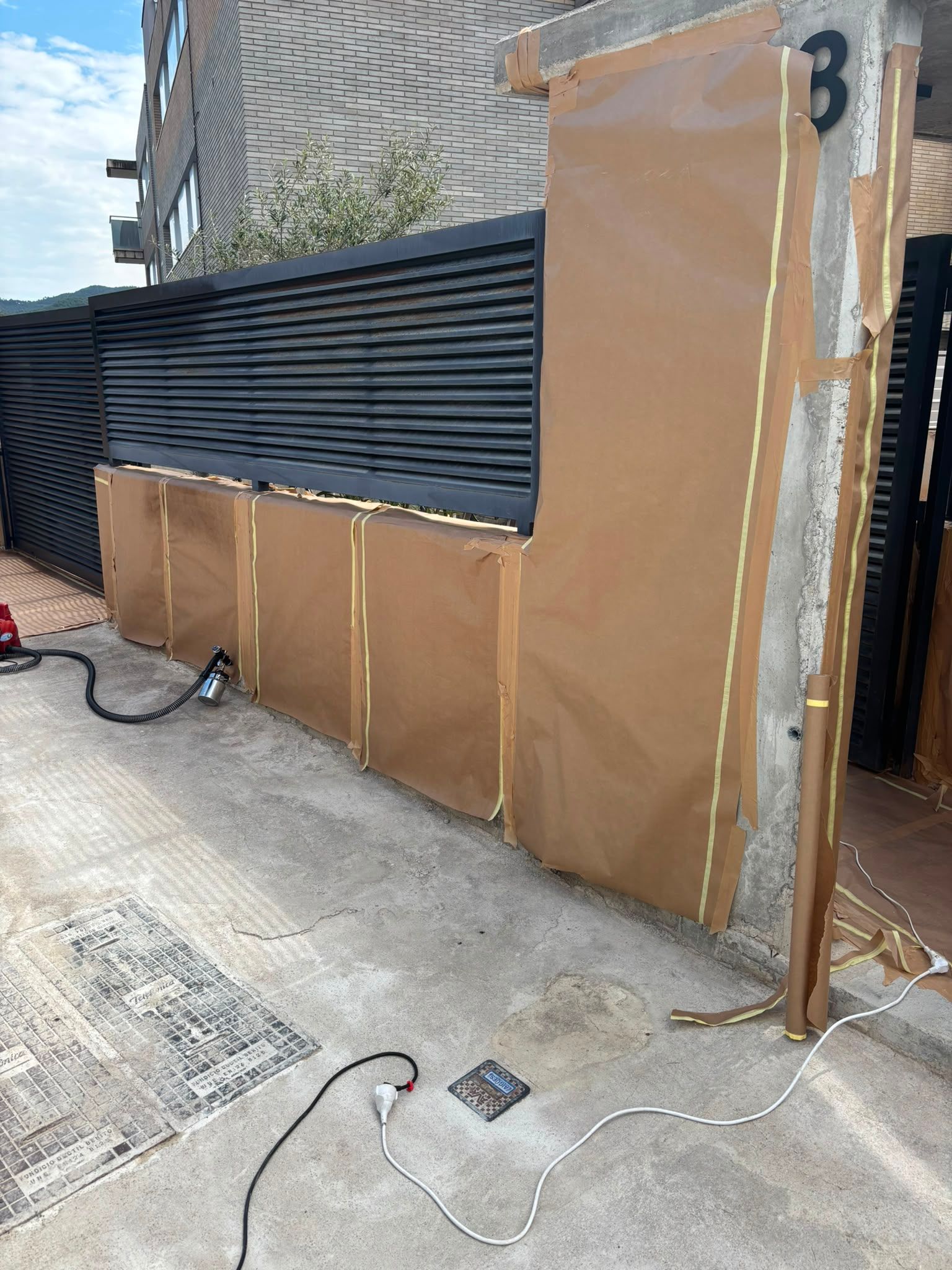 Paneles de pared marrones temporales y vallas negras junto a una entrada de vehículos y una acera frente a una casa.