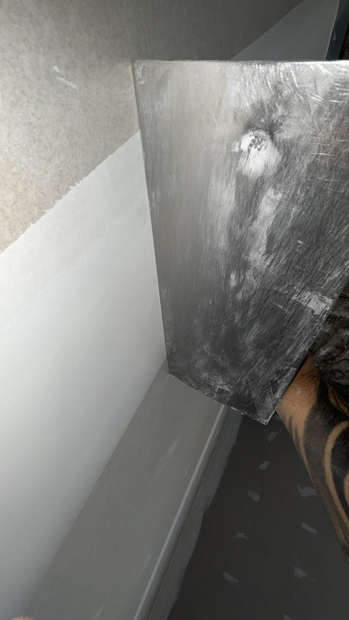 Un panel plateado sucio apoyado contra una pared gris en un pasillo estrecho.